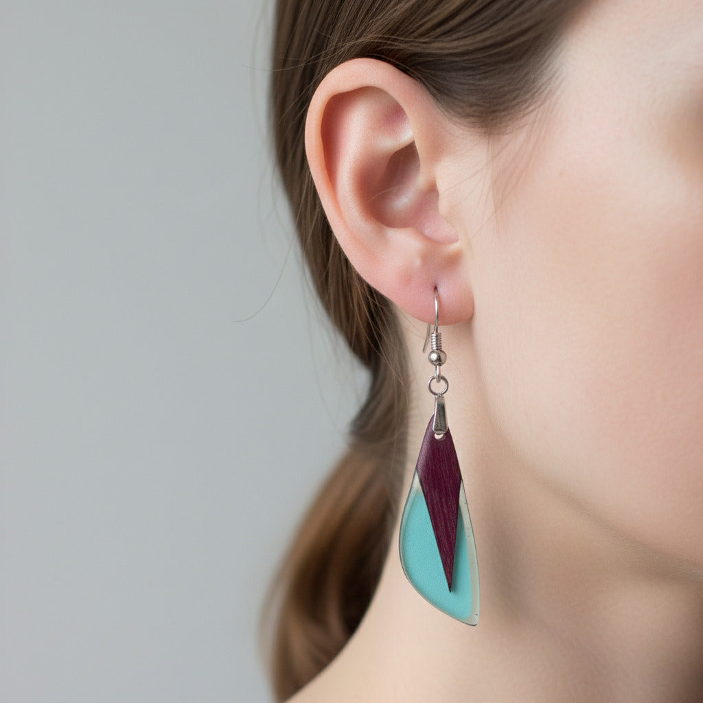 pendientes de madera de amaranto y resina azul claro transparente pulido en alto brillo, con fornitura de acero inoxidable 316. El pendiente está puesto en una oreja de modelo