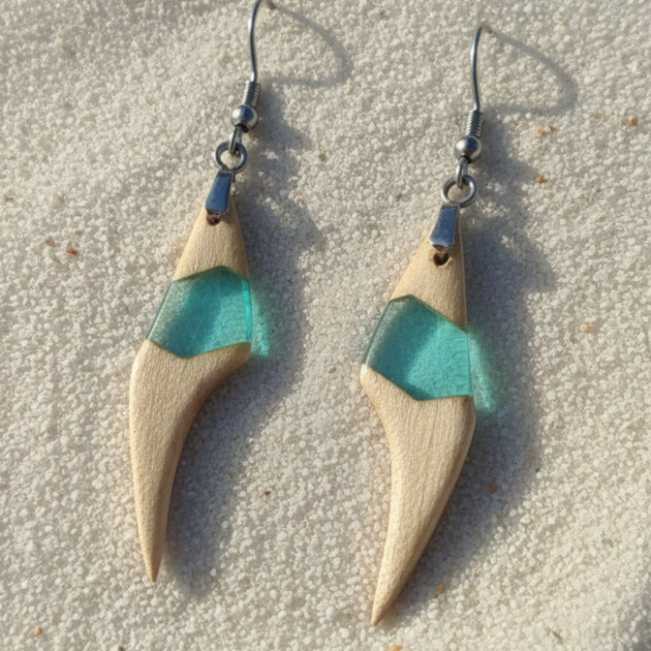 pendientes de madera de arce y resina azul claro translúcido con enganche de acero inoxidable sobre fondo de arena de mar